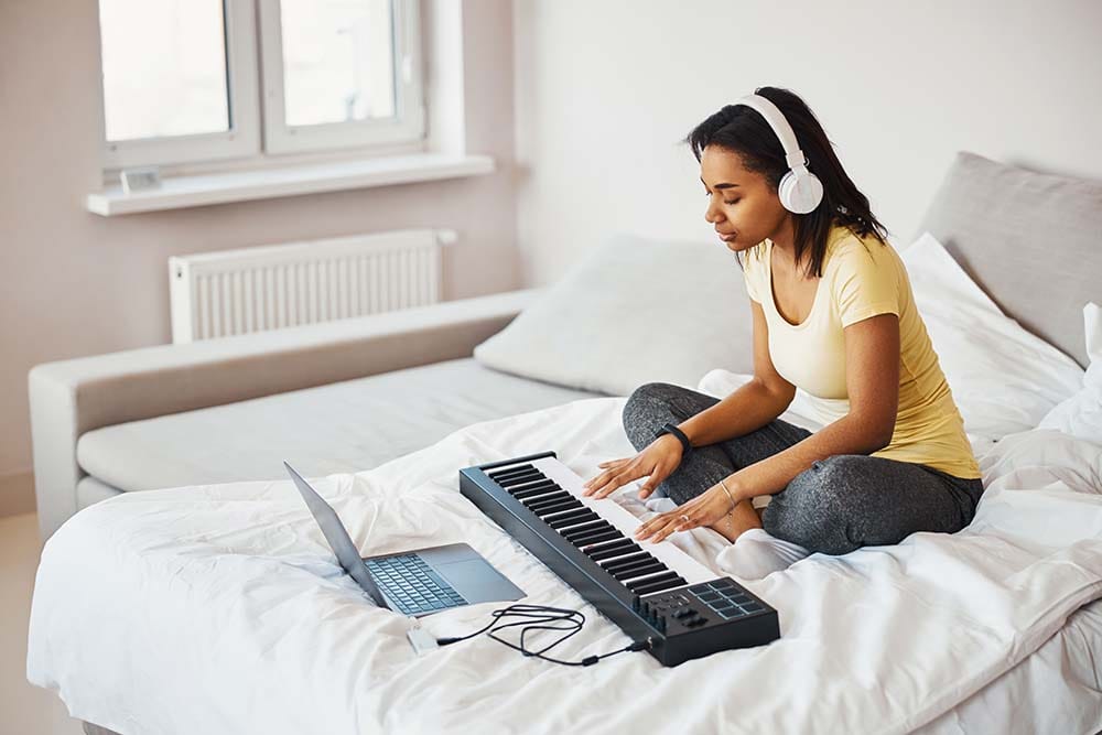 A female producer trying to make music on her computer while sitting on her bed.
