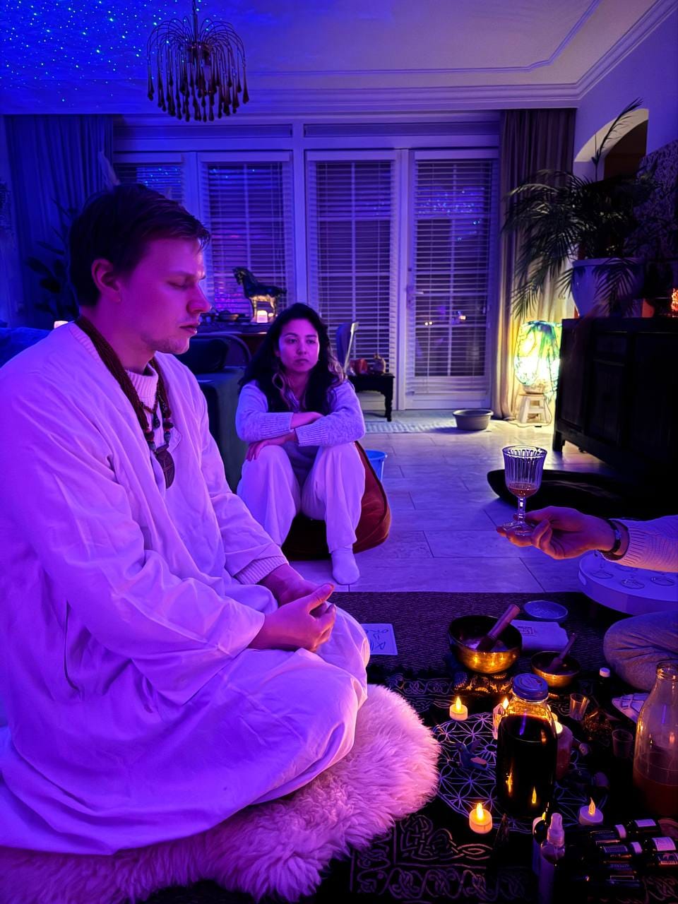 Ruben seated in the ceremony space, receiving a cup, candlelight