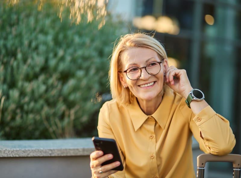 Woman in a yellow shirt smiling with her phone outdoors