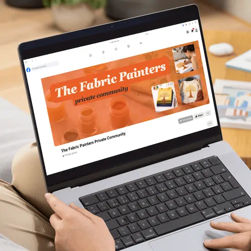 Person using a laptop to view "The Fabric Painters Private Community" group page, featuring images of fabric painting and art supplies in the banner.