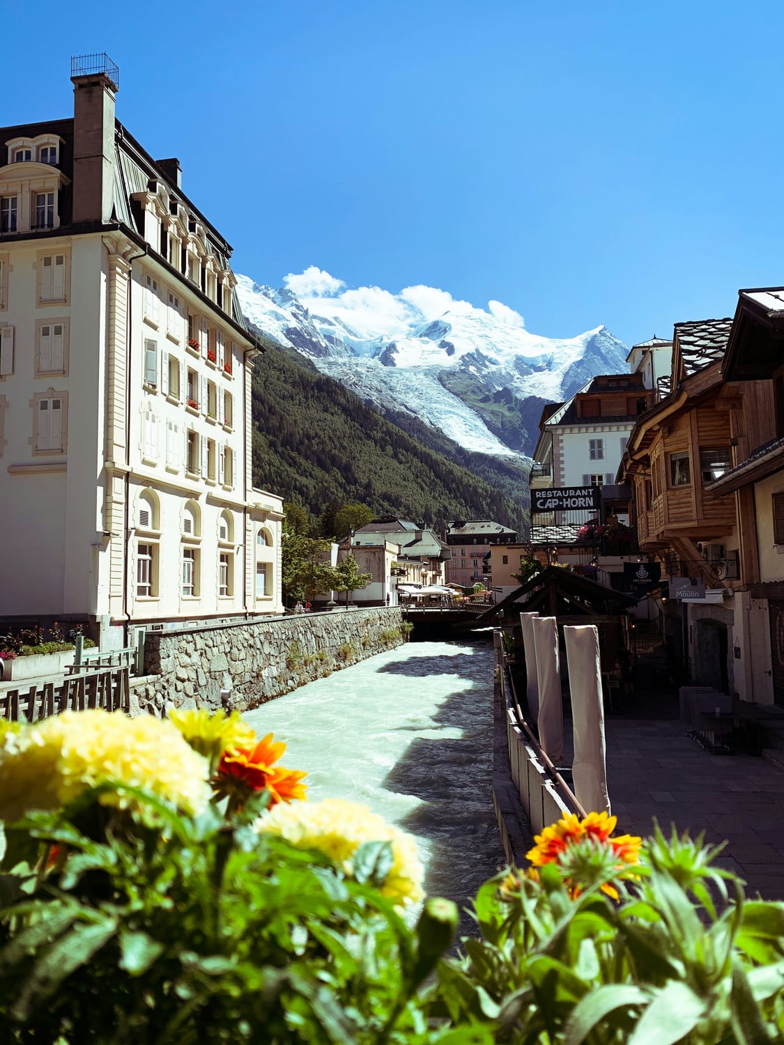 Scene from a French mountain village flanking an alpine stream with a surging glacier rising in the background