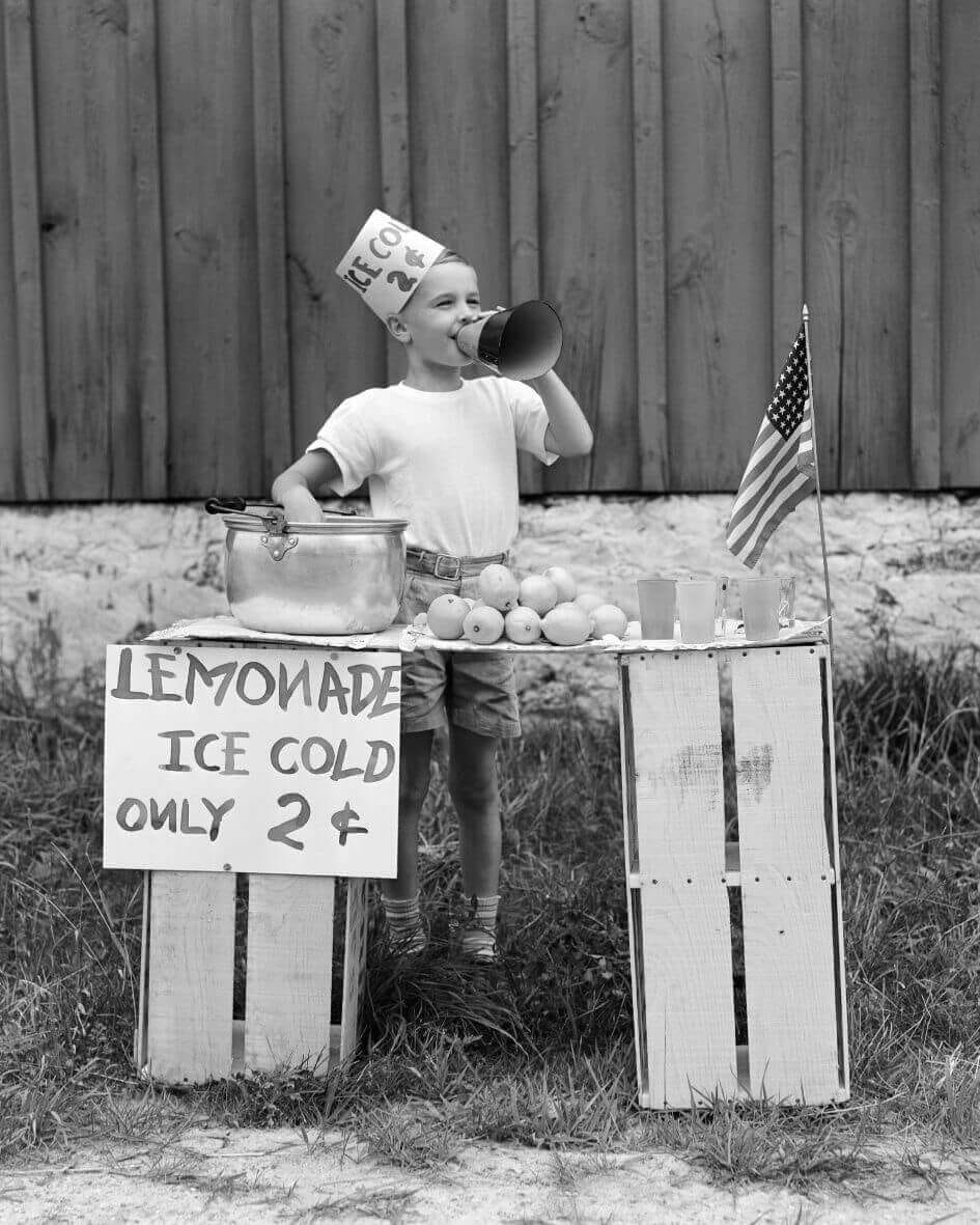 Junge mit Zitronen verkauft Limonade an einem Lemonade Stand.