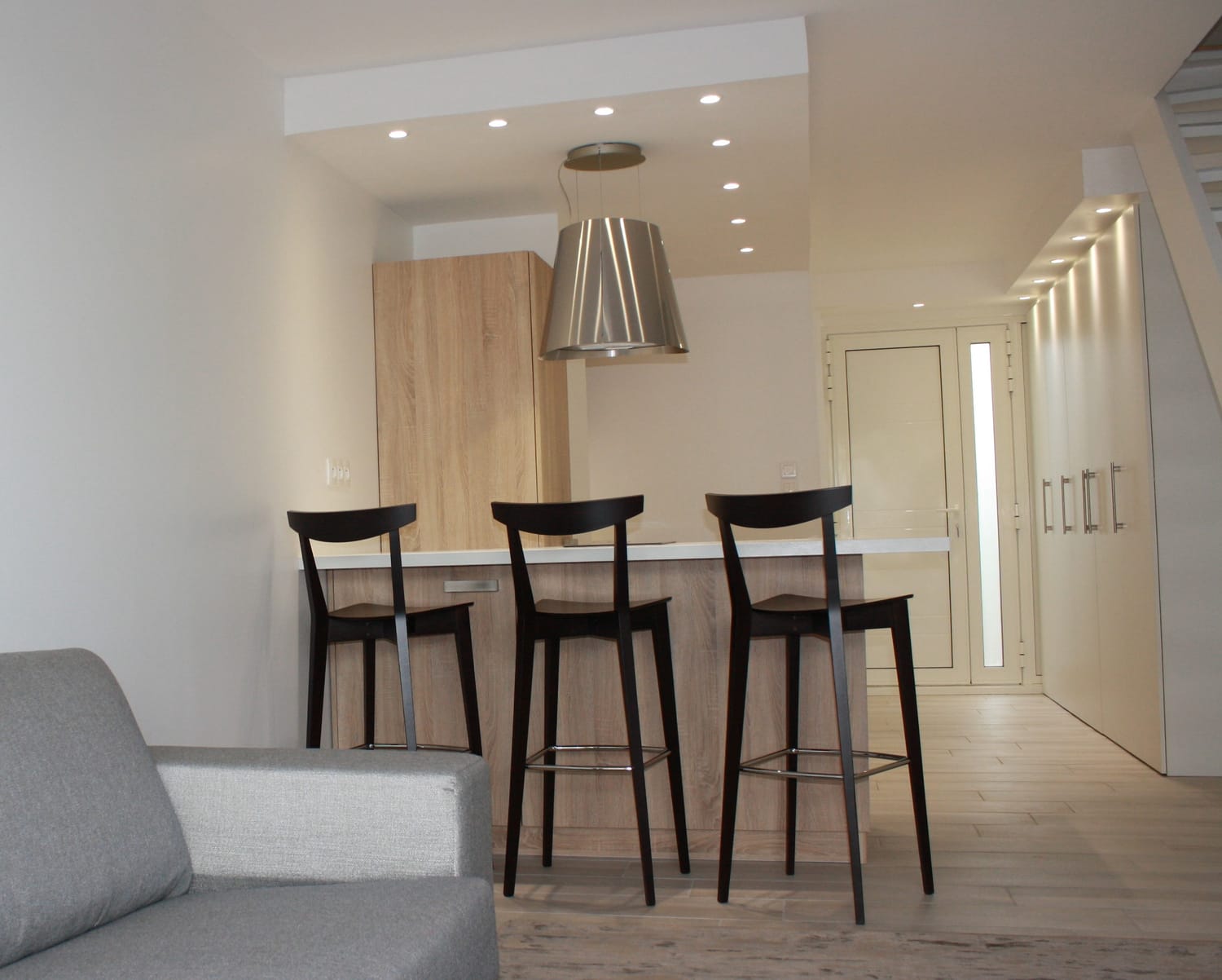 cuisine ouverte bois clair rénovée Marina Port Camargue / îlot bar tabourets noirs et salon lumineux / rénovation appartement bord de mer Gard