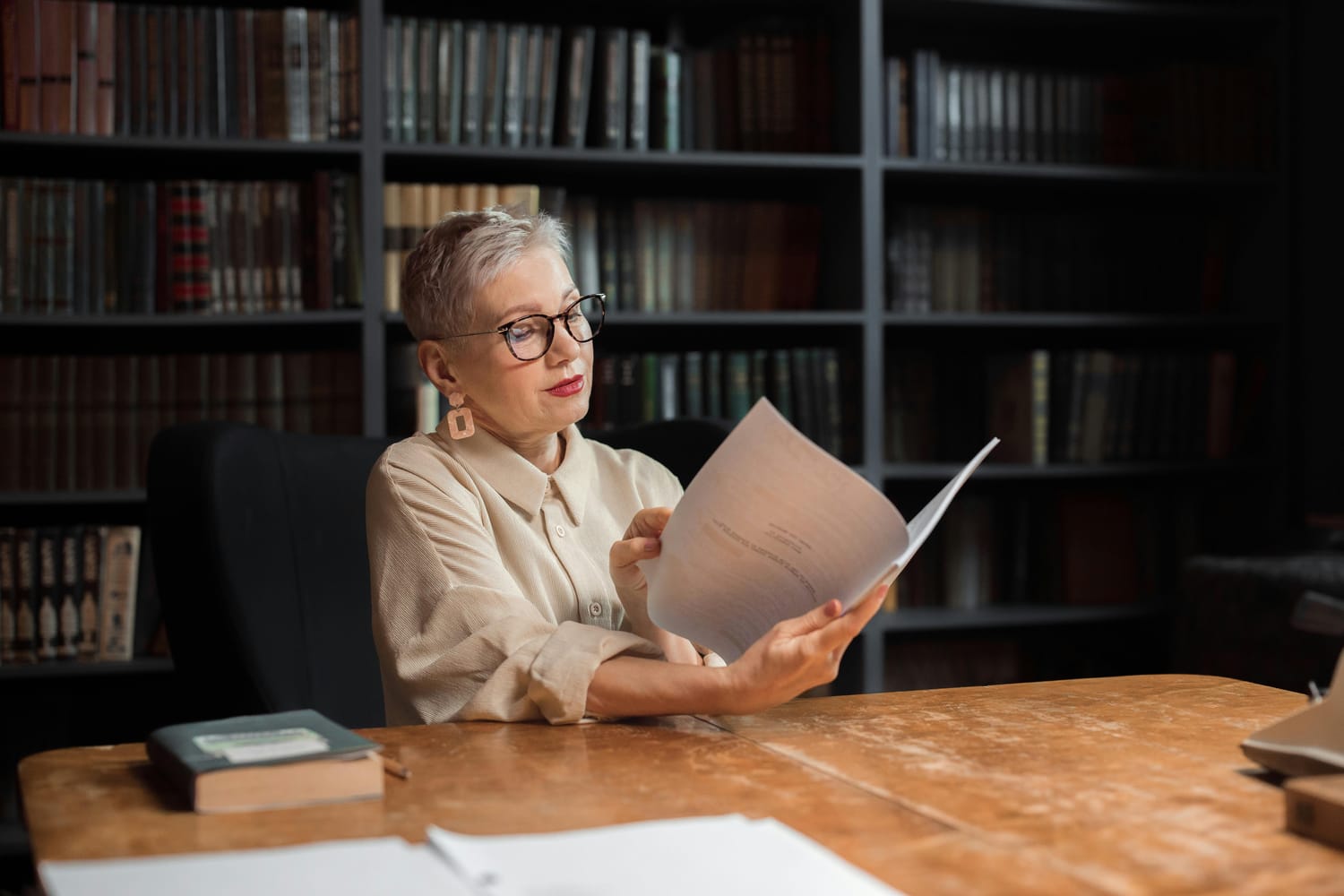A woman with gray hair and glasses sitting at a table reading a document