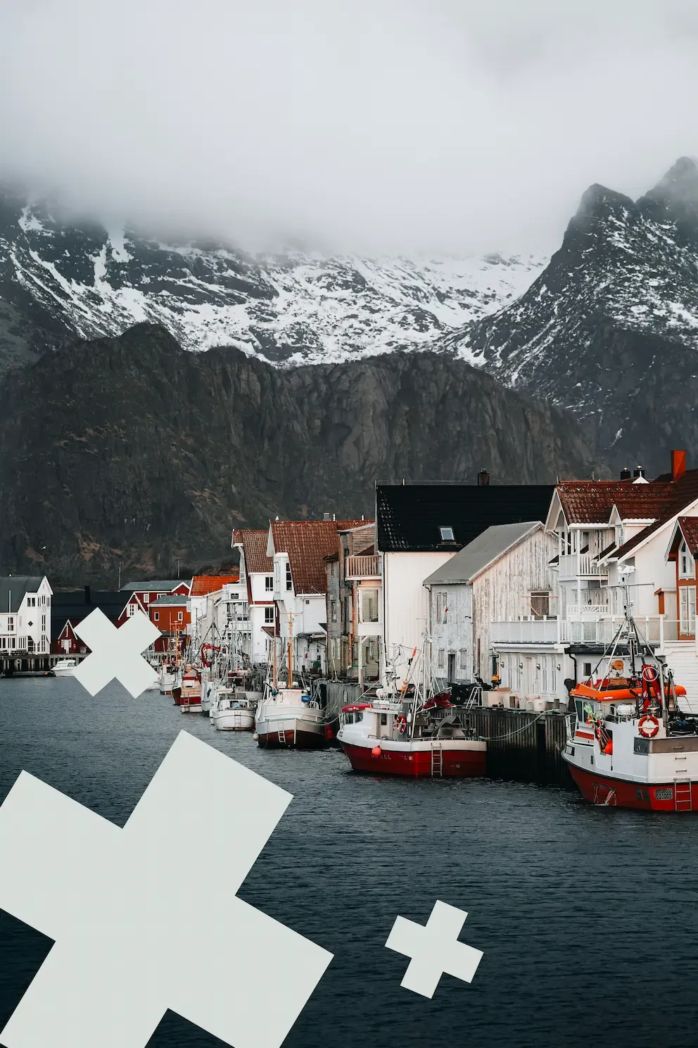 oastal harbor with fishing boats and wooden houses beneath snow-capped mountains