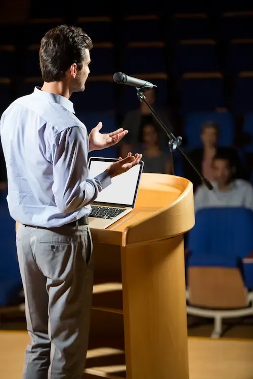 Speaker presenting at a podium with a microphone to an audience