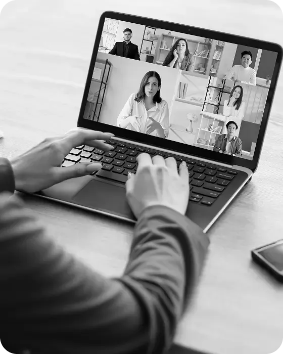 Hands typing on a laptop keyboard during a virtual business meeting with a team on the screen.