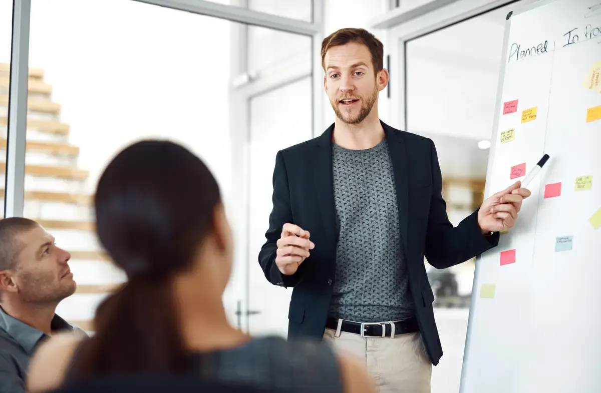 Man presents a pitch deck's key points on a whiteboard during a team meeting in a modern office.