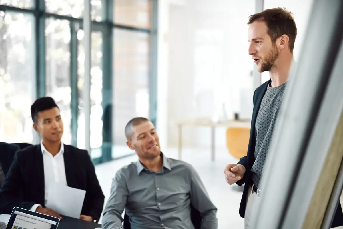 A group of men participating in a business presentation, likely a startup pitch deck with slides, in an office environment.