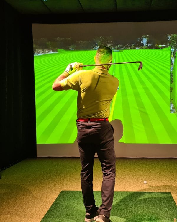 A golfer swinging in an indoor golf simulator bay