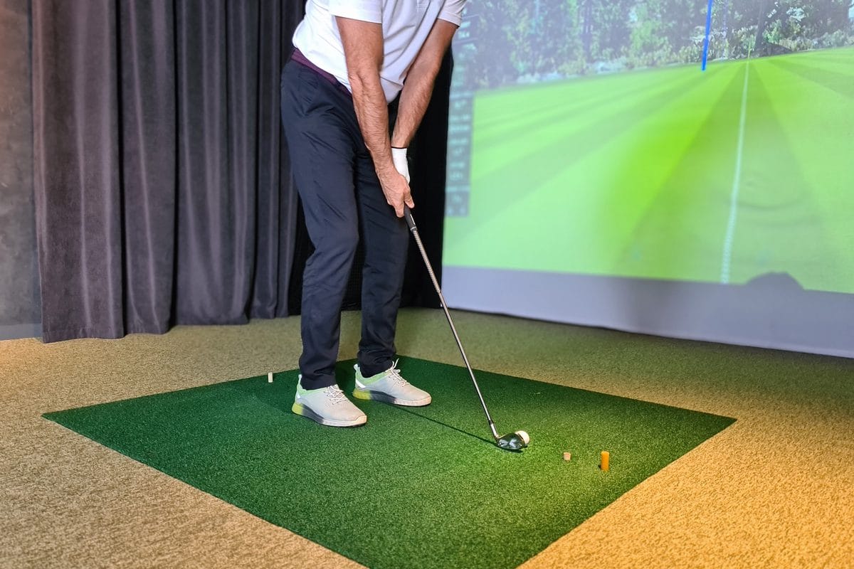 A golfer at address on a green hitting mat with the impact screen ahead