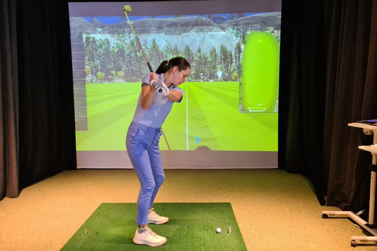 A golfer swinging in a home simulator bay with side curtains