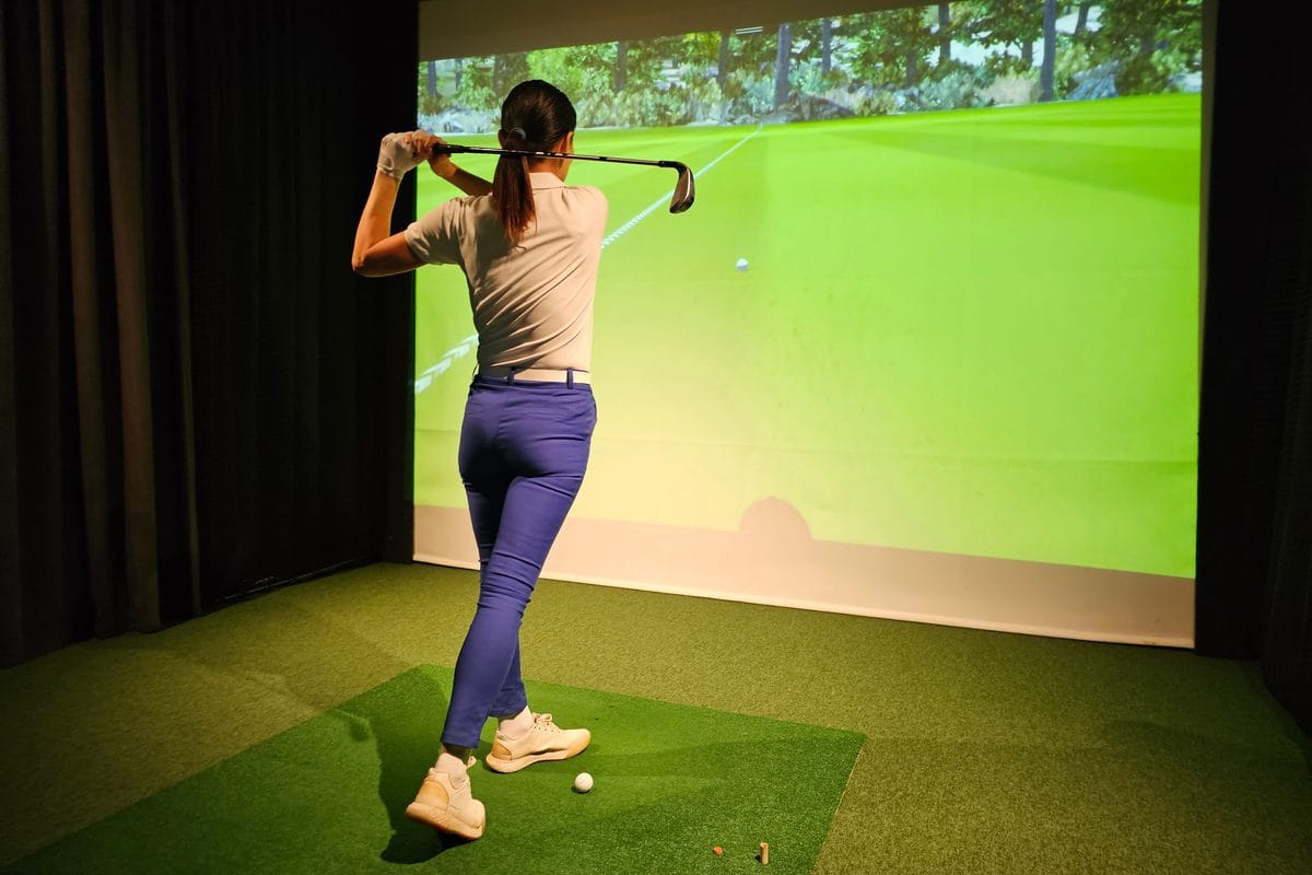 A golfer mid-swing in a home simulator bay with a projected fairway on the impact screen