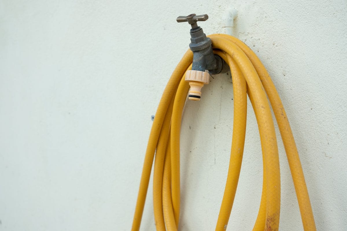 An outdoor water tap with a coiled garden hose on an exterior wall