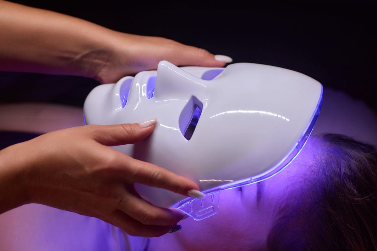 A white LED face mask glowing purple, held over a person's face