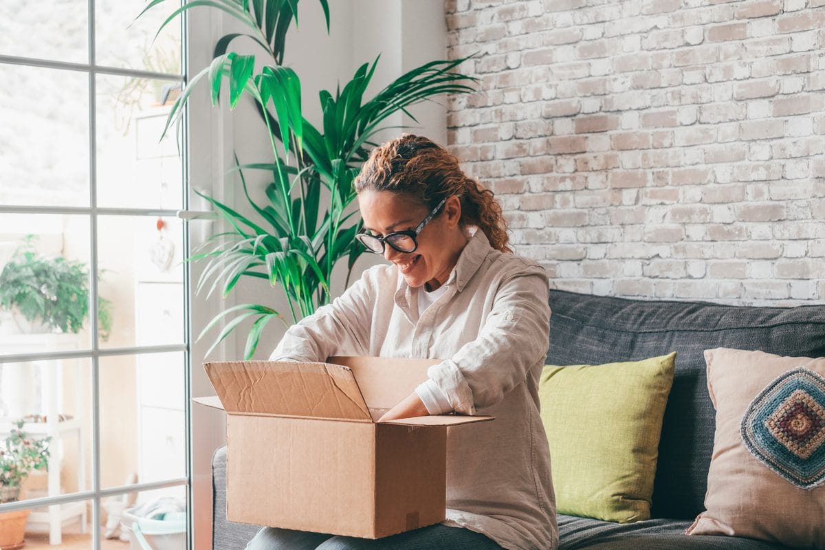 A woman opening a cardboard delivery box on her sofa