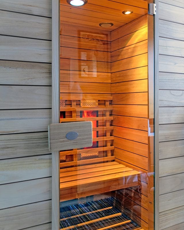 An infrared sauna cabin with a glass door and glowing heating panels