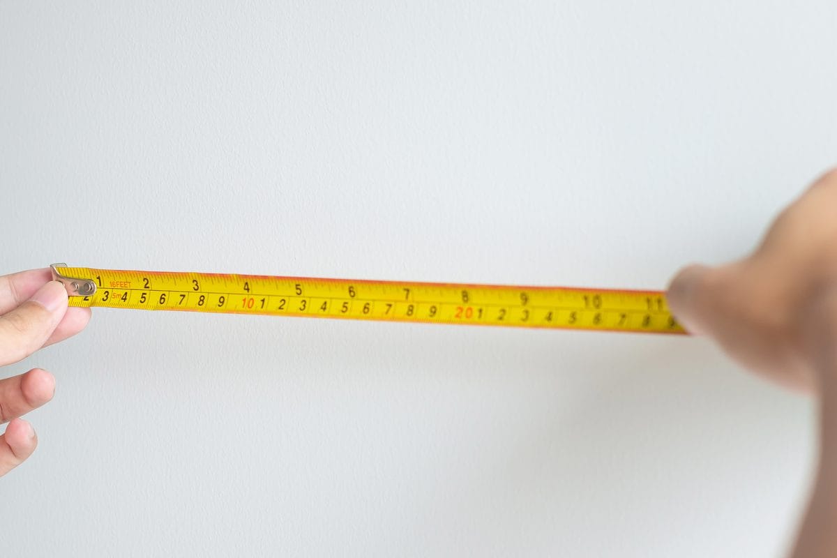 Two hands stretching a tape measure across a white wall