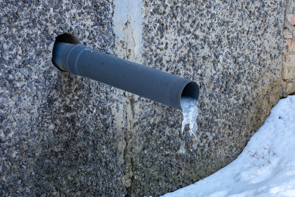 Ice forming at the end of a plastic pipe on an outside wall in snow
