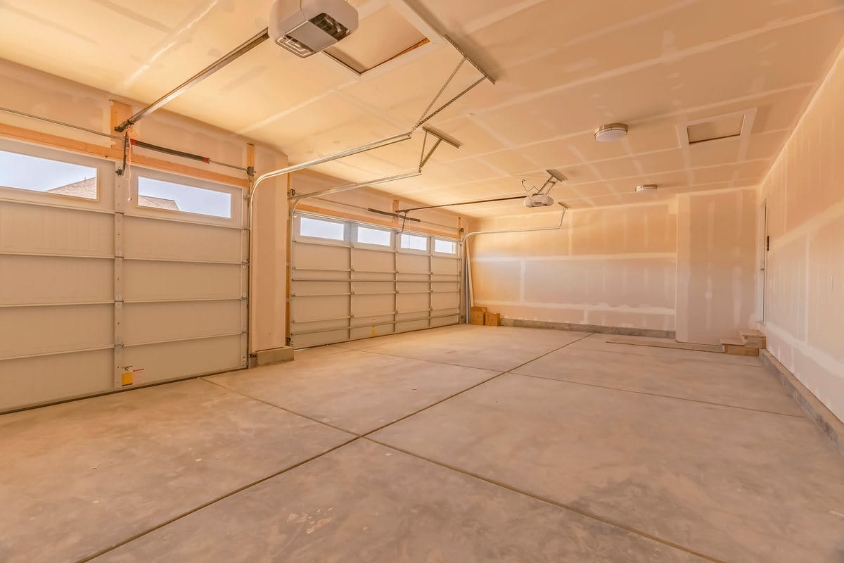 An empty two-car garage with unfinished drywall and a ceiling-mounted opener for each door