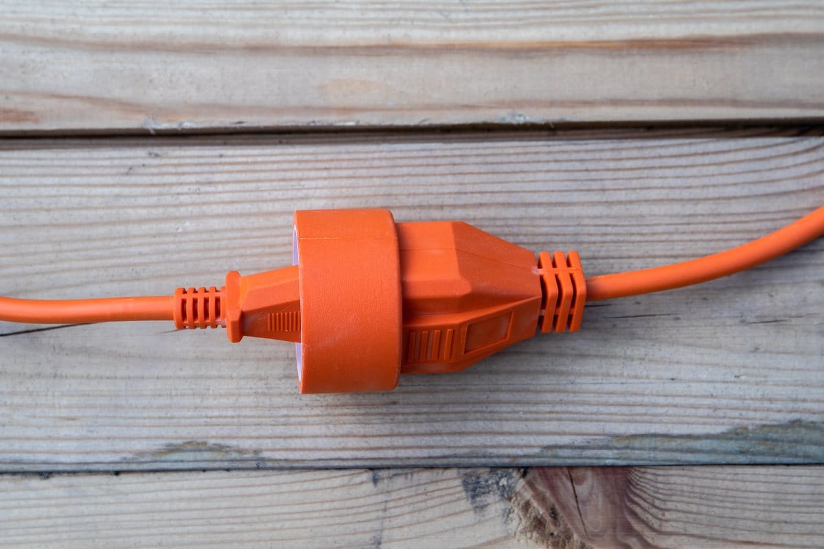 An orange extension cord joined to a plug, lying on weathered wood boards