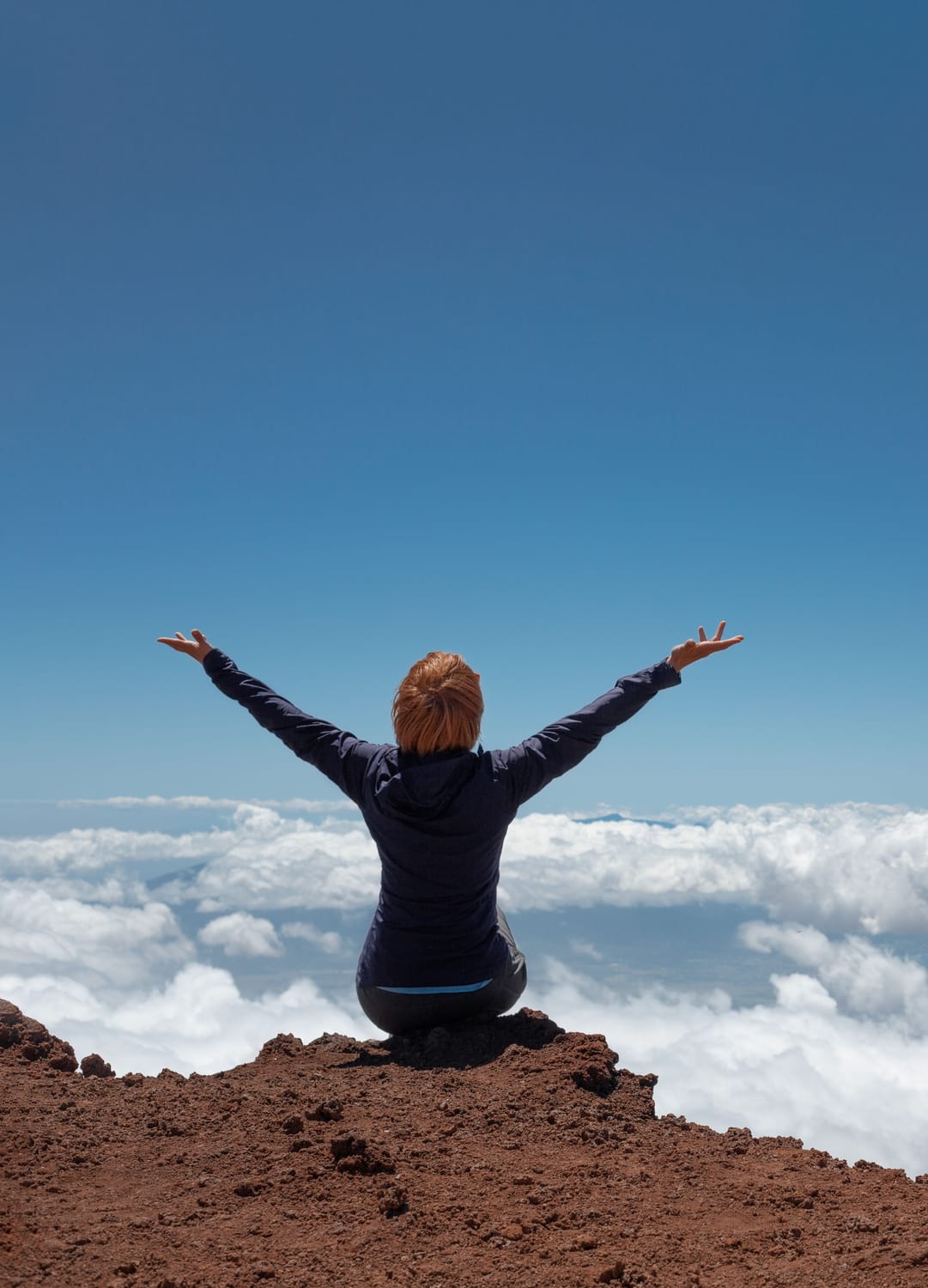 Femme bras ouverts au sommet d'une montagne, au-dessus des nuages