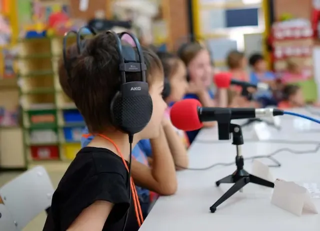Niños sentados en una mesa con audífonos y micrófonos