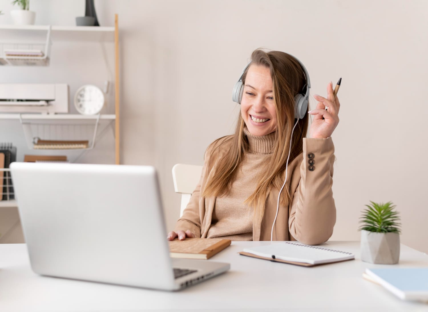 Femme souriante assise à un bureau face à un ordinateur portable, un casque sur les oreilles