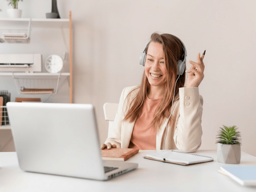 Femme souriante assise à un bureau face à un ordinateur portable, un casque sur les oreilles