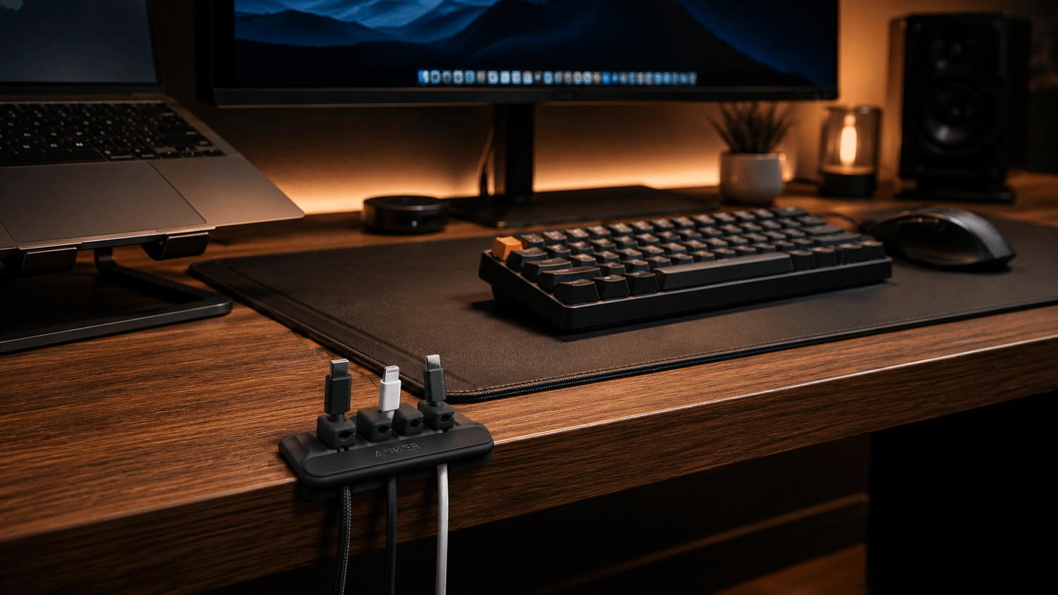 A clean and minimalist home office desk setup featuring a large black premium desk mat with a compact mechanical keyboard and ergonomic wireless mouse neatly arranged on top. The workspace includes warm ambient lighting, a wooden desk surface, a laptop on a stand, a widescreen monitor with soft backlighting, organized cable management, and modern desk accessories like a small plant and coffee mug. The cozy creator-style setup has cinematic shadows, a premium productivity aesthetic, and a clutter-free work-from-home atmosphere.