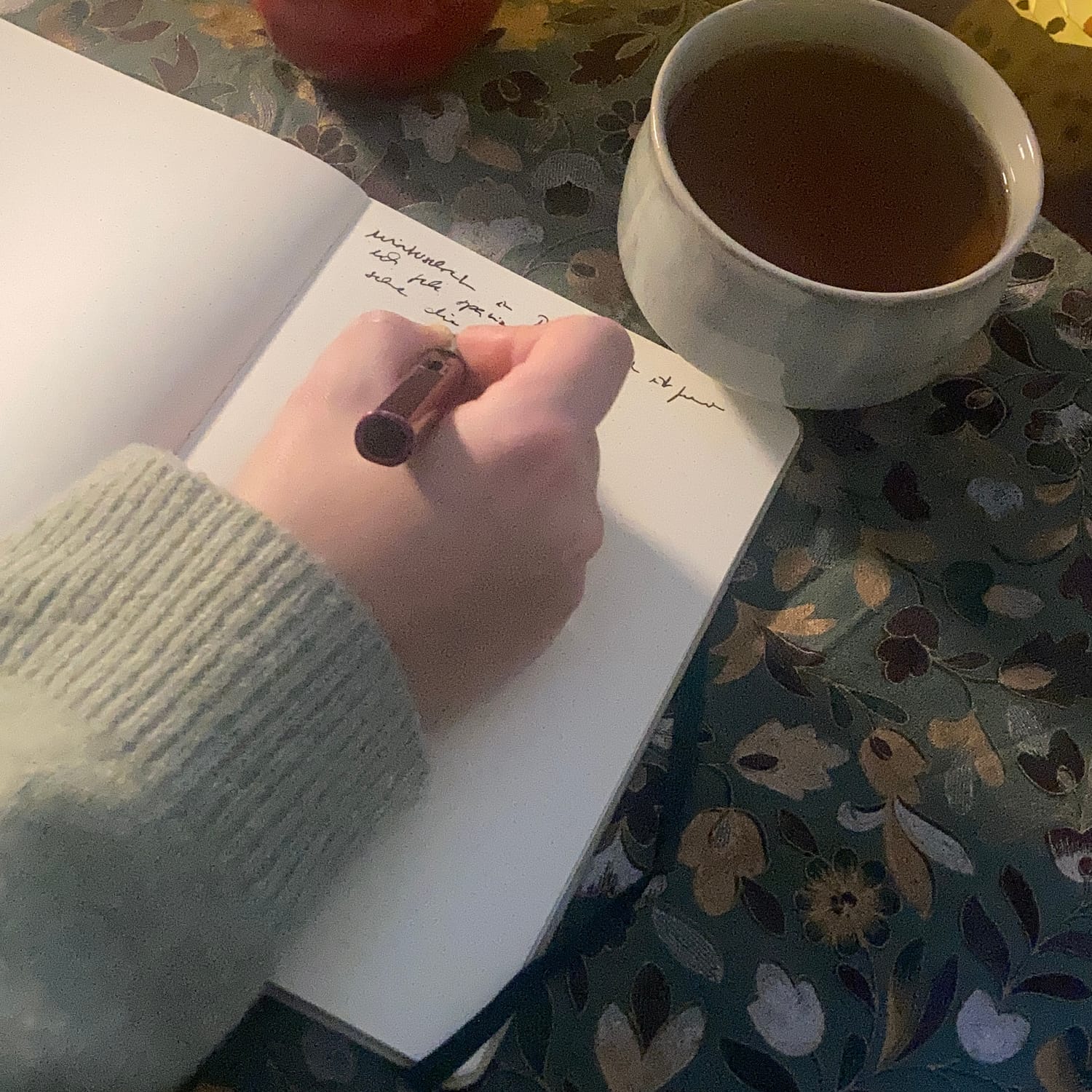 Eine Hand beim achtsamen Schreiben in ein Journal mit einer Tasse Tee.