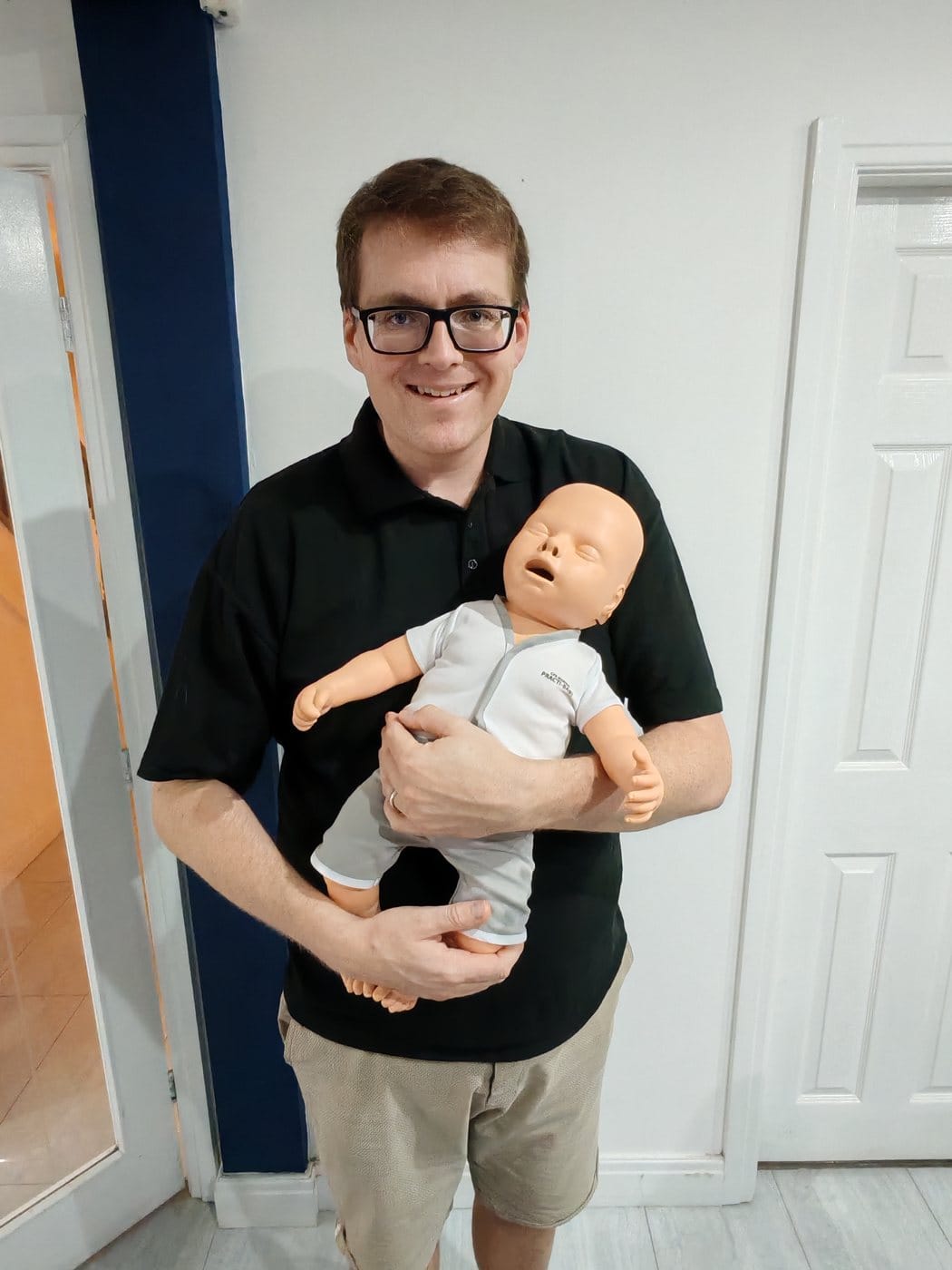 James smiling while holding an infant training manikin