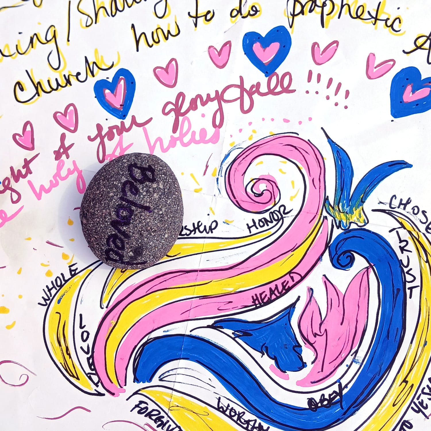 Art by Elissa: a stone painted with the word Beloved, resting on hand-lettered words and swirls of pink, gold and blue