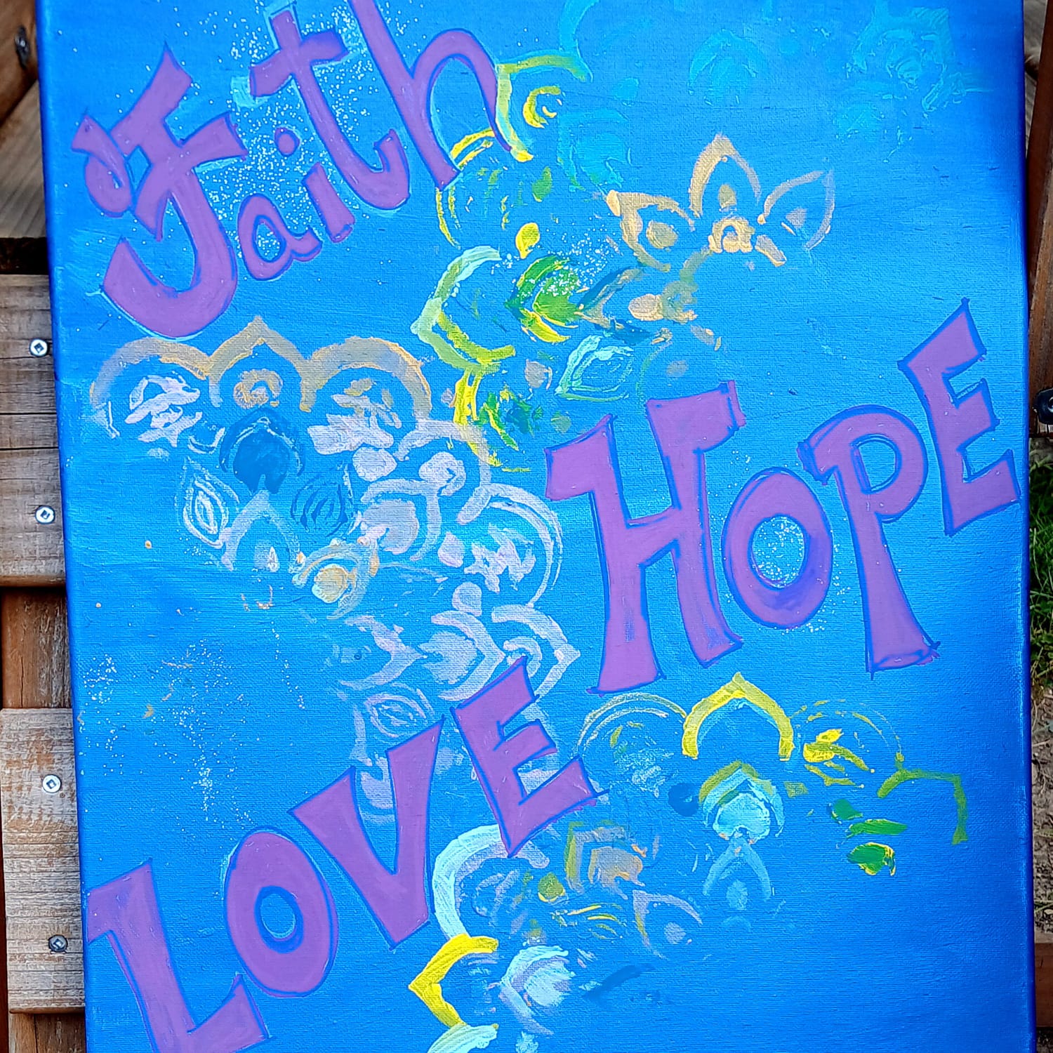 Painting by Elissa: the words Faith, Hope and Love in purple on blue, with gold and white flowers