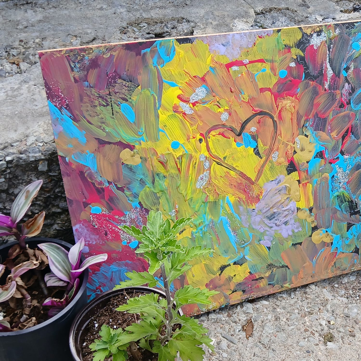 Painting by Elissa: swirls of rainbow color around a heart, propped on a step between potted plants