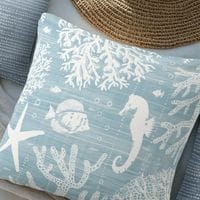 a light blue throw pillow in coastal style featuring a white block printed seahorse and fish design.