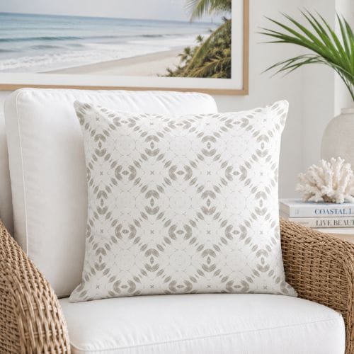 A white modern coastal throw pillow with a neutral geometric pattern on a white cushioned rattan armchair.