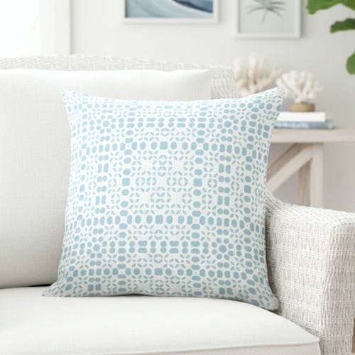 A light blue and white coastal throw pillow on a white rattan sofa.