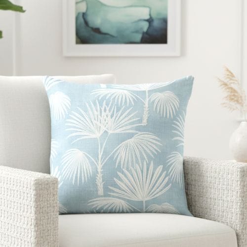A Modern Light Blue Palm Tree Coastal Throw Pillow on a white armchair