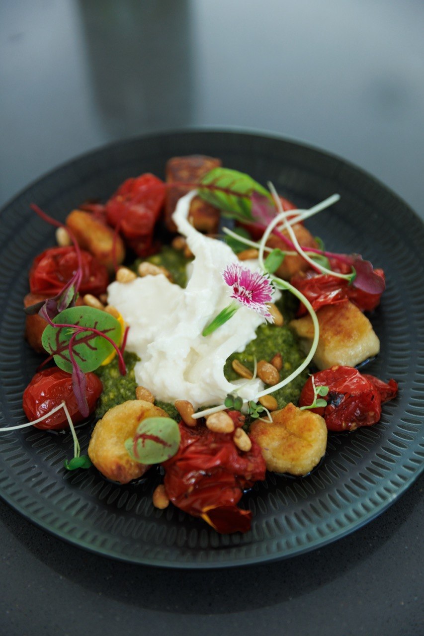 Plat gastronomique dressé avec sauce verte, gnocchis et fleur comestible