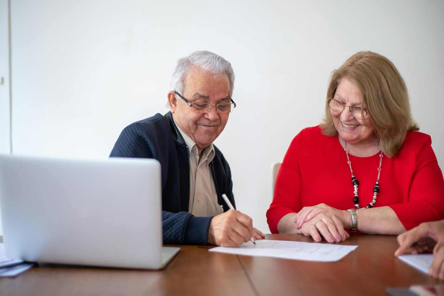 Husband and wife signing document on desk with a laptop