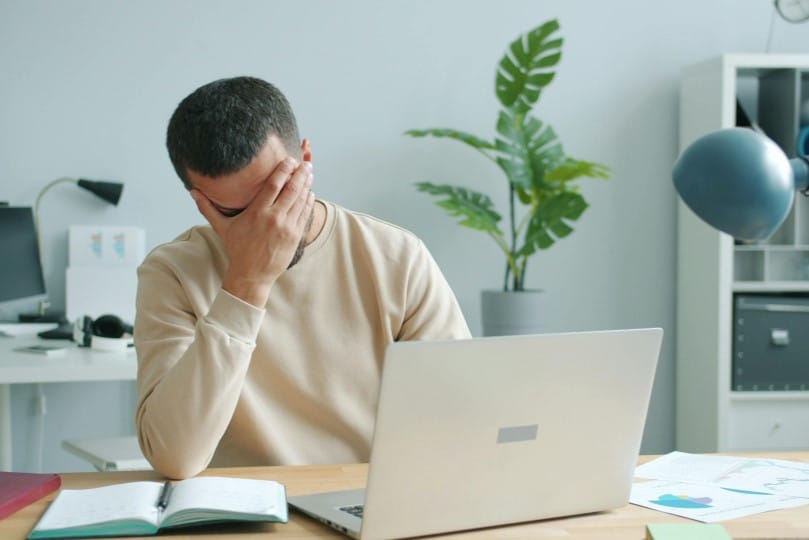 Frustrated business owner with hand over his face at desk with his laptop