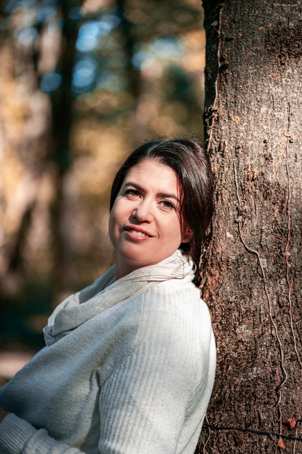 Manuela Pulkert, lächelnd an einen Baum gelehnt im herbstlichen Wald