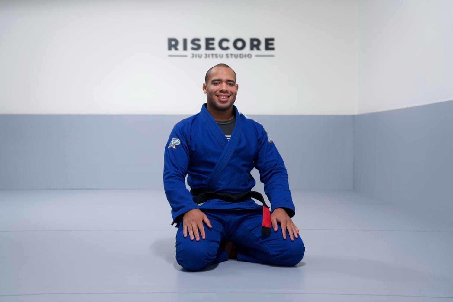 Portrait of Johnatha kneeling on the mat in a blue gi, smiling