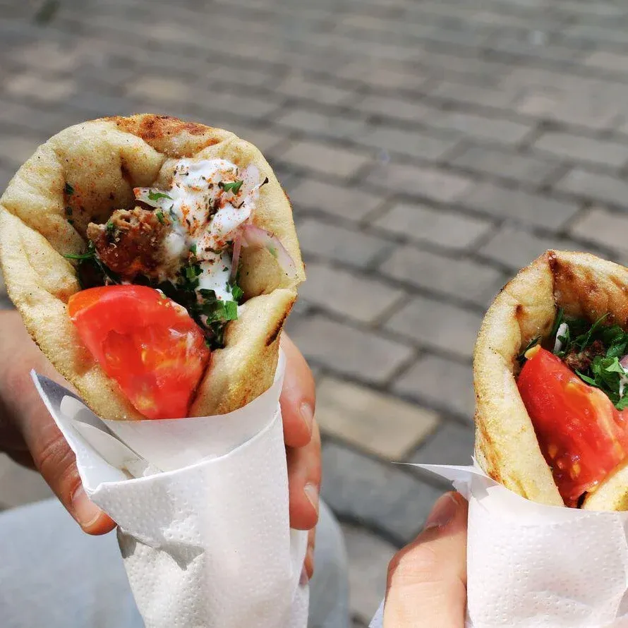 Two souvlaki pittas held up over a cobbled Athens street