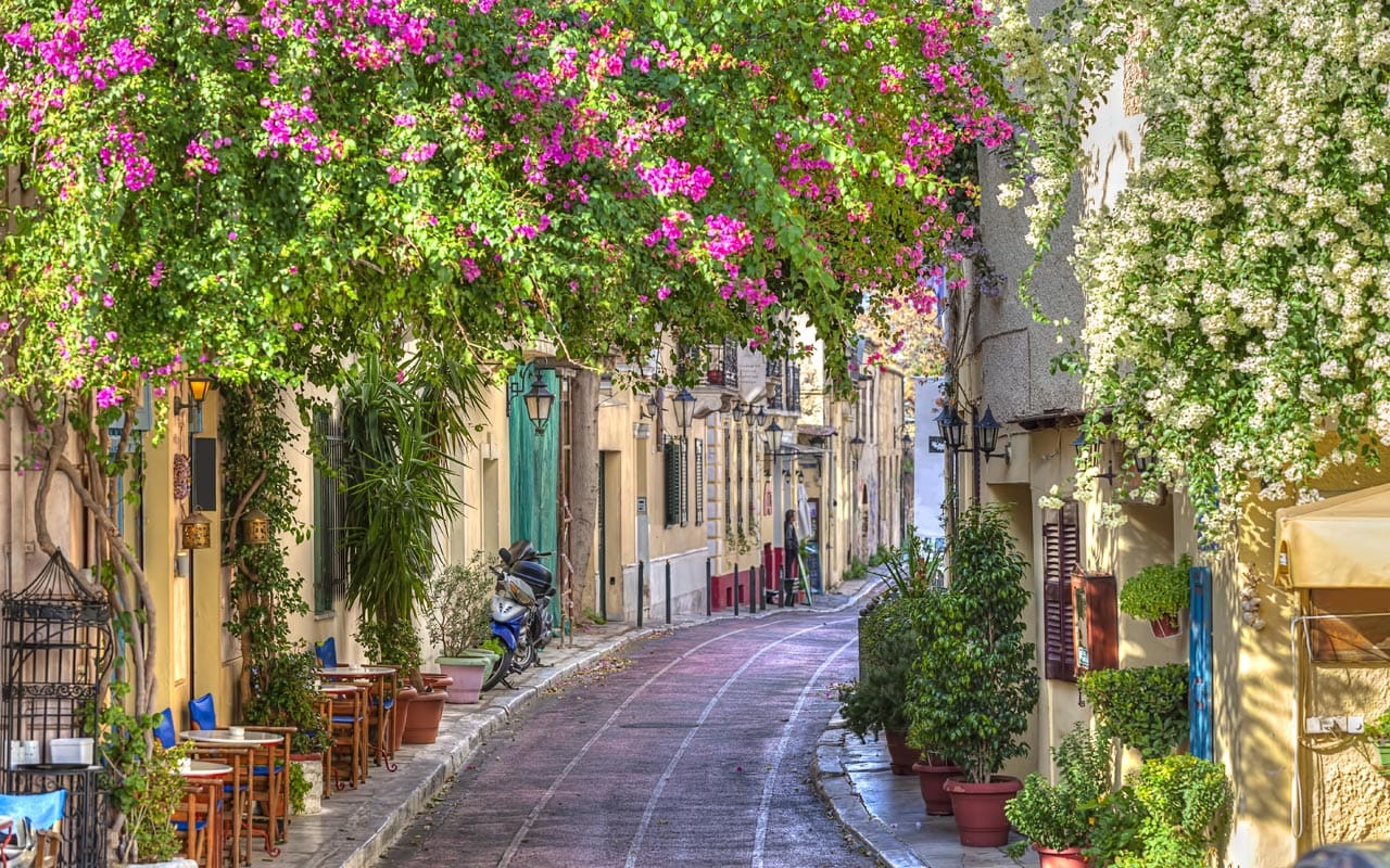 Quiet Athens street with bougainvillea, greenery and small café tables