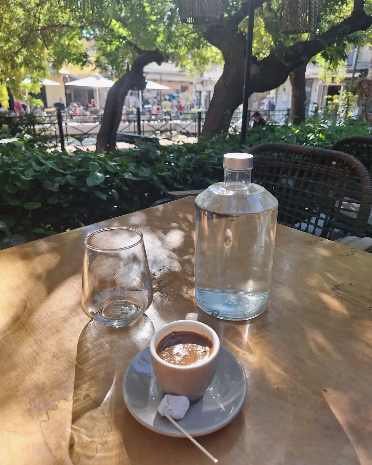 Greek coffee with a loukoumi on the saucer, a glass and a bottle of water on a sunlit café table under the trees