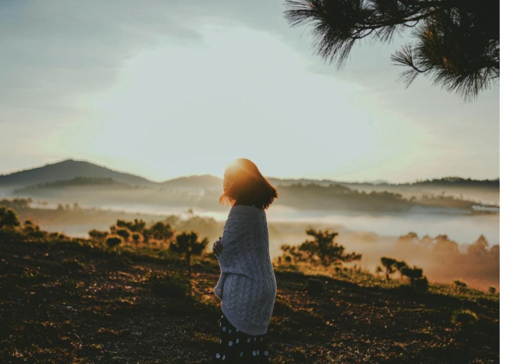 Woman standing alone looking out over misty hills at sunset