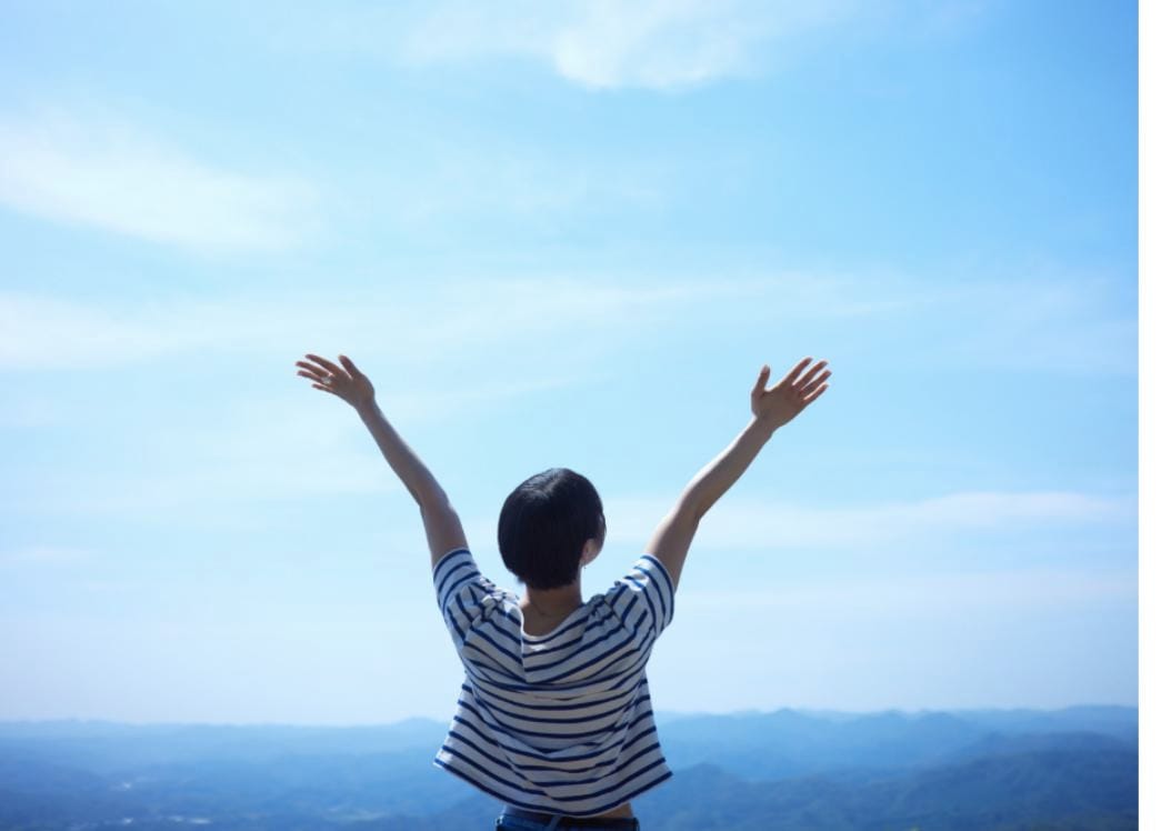 Woman standing with arms raised in freedom overlooking misty mountains