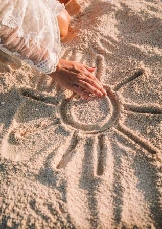 Main de Shanna dans le sable dessinant un soleil